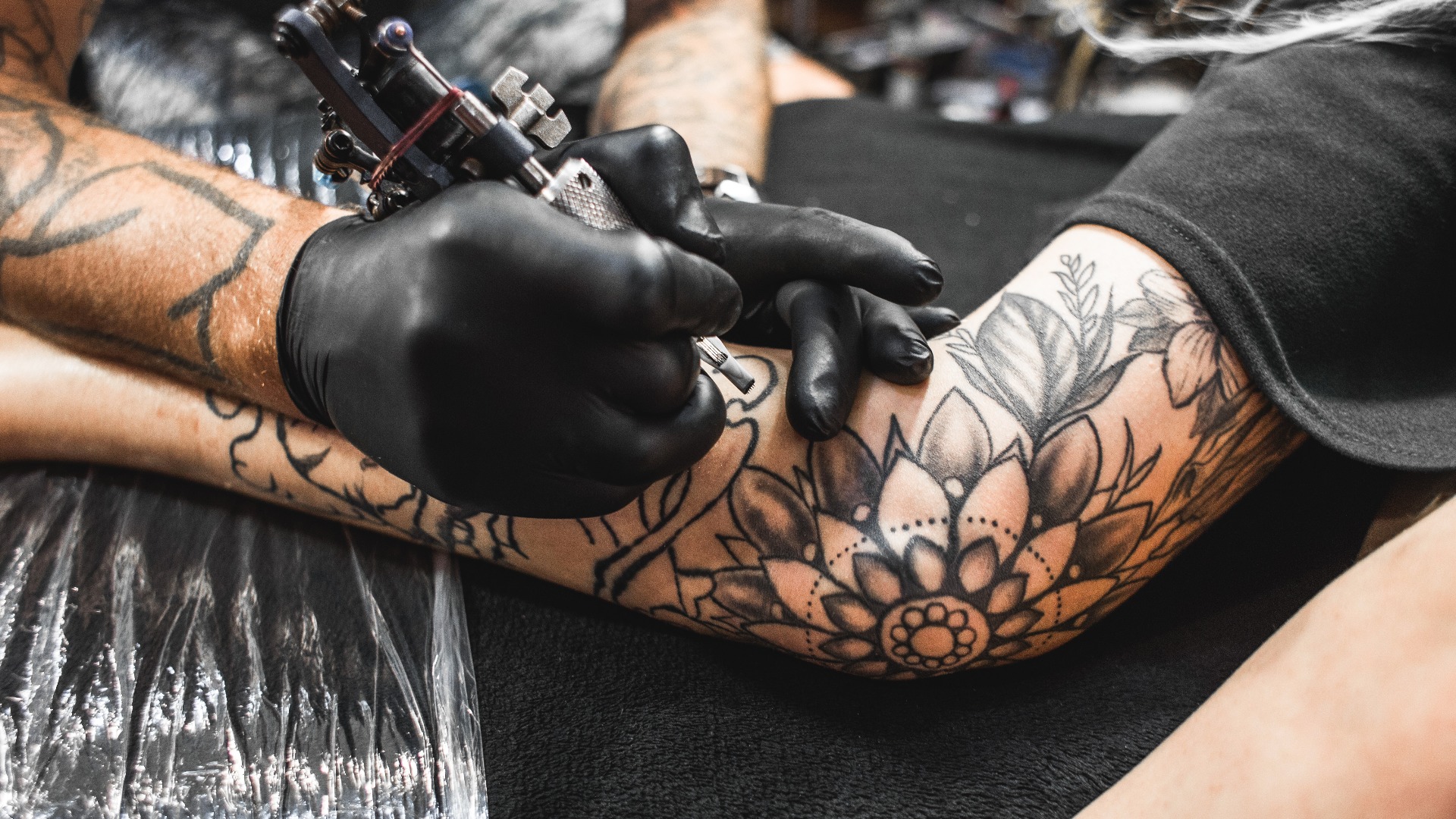 Mädchen mit Dreadlocks in einem Tattoo-Studio. Der Meister erstellt ein Bild auf dem Körper eines jungen, schönen Mädchens. Nahaufnahme von Händen und Tattoo-Maschine