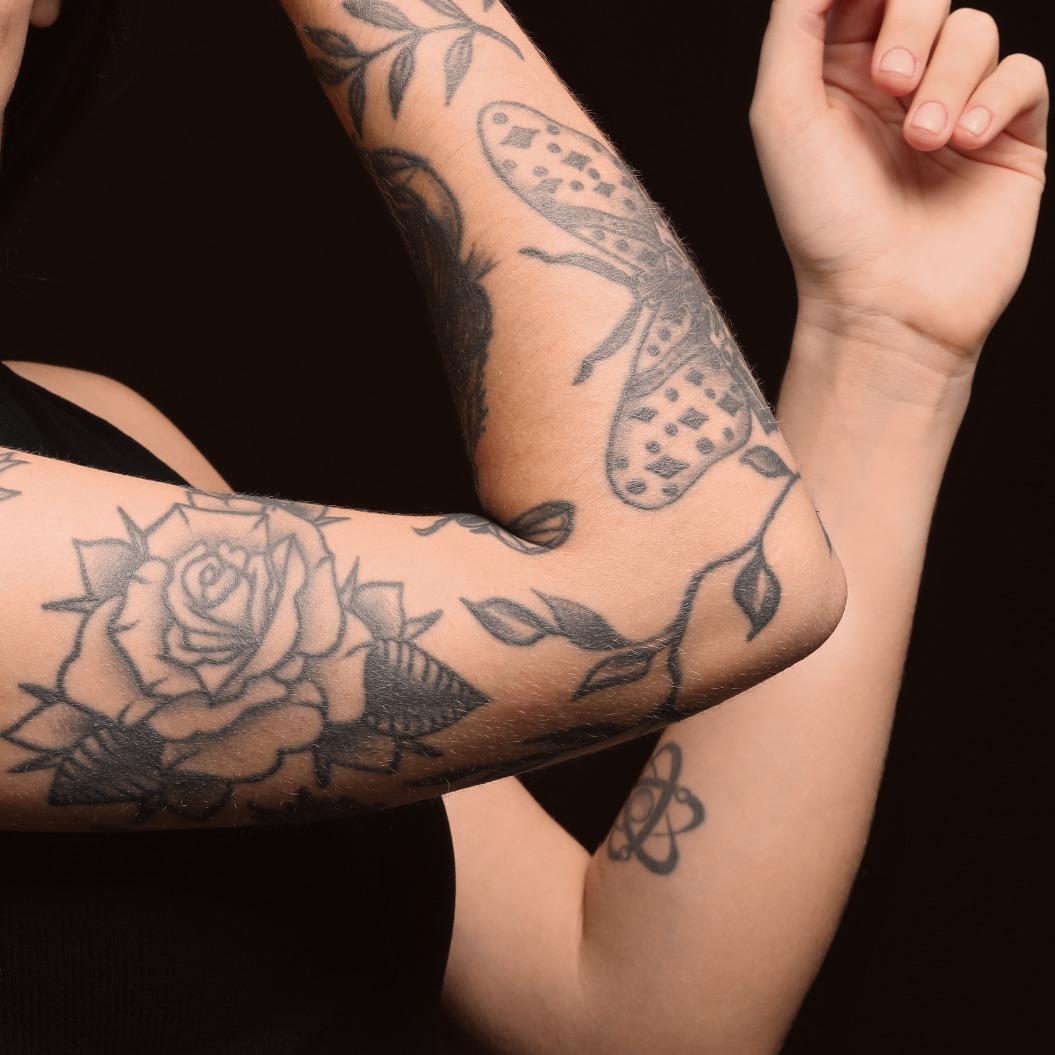 Schöne Frau mit Tattoos auf den Armen vor schwarzem Hintergrund. Platz für Text